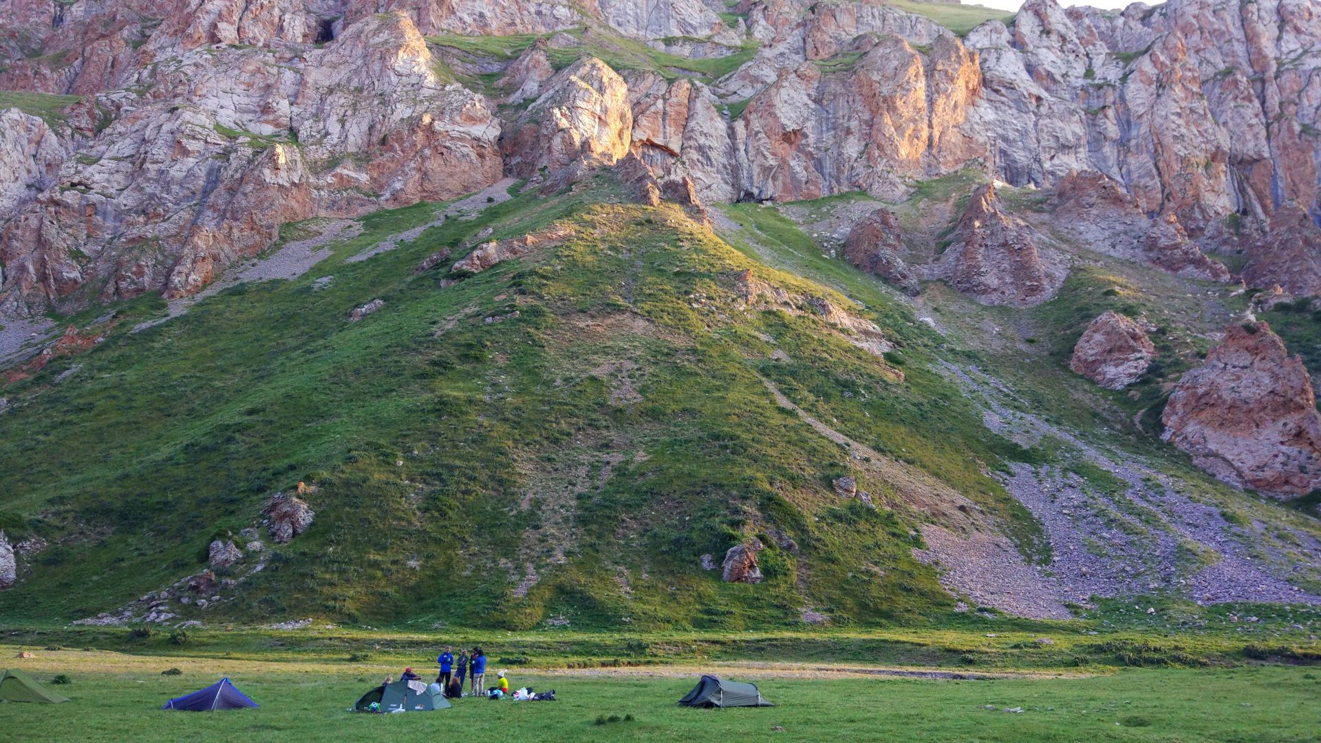 Small tents pitched on a meadow below red rock cliffs (partner-supplied Kyrgyzstan photo)