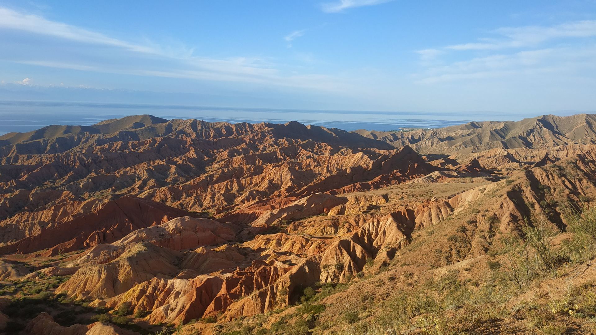 Red and ochre eroded hills with a large lake on the horizon (partner-supplied Kyrgyzstan photo)