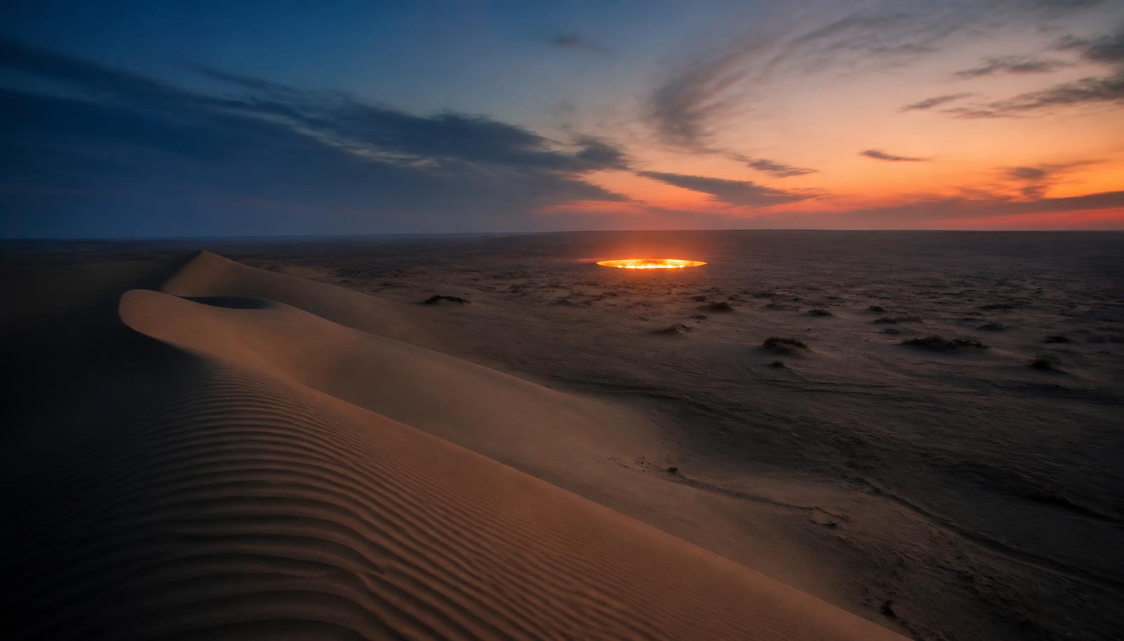 Karakum desert dunes at dusk with the glow of the Darvaza gas crater on the horizon