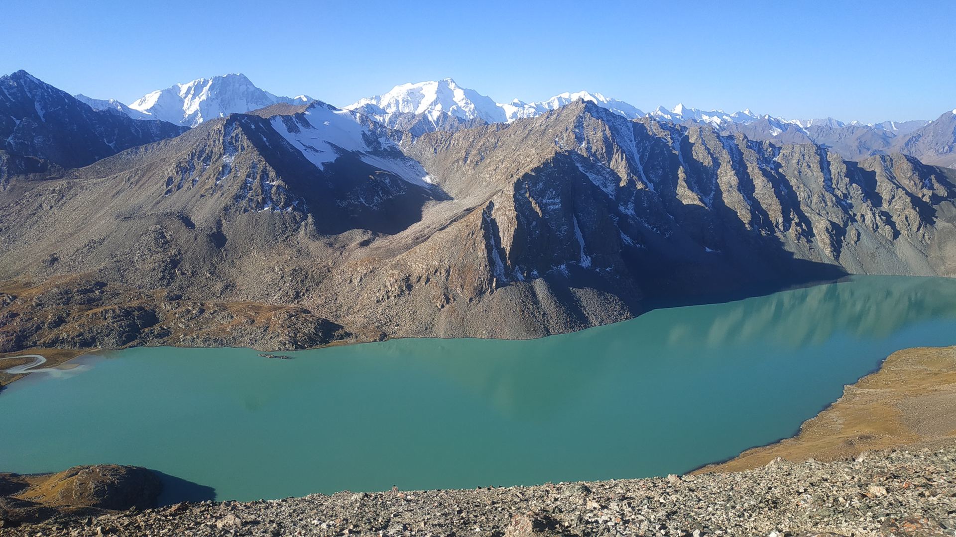 Turquoise mountain lake beneath bare ridges and snow-capped peaks (partner-supplied Kyrgyzstan photo)